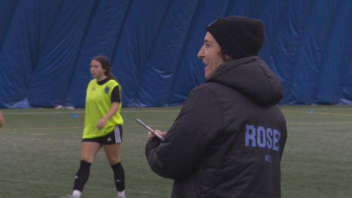 Une femme, aux abords du terrain, évalue des joueuses de soccer.