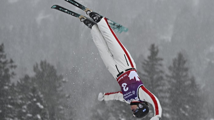 Une skieuse acrobatique en blanc fait des figures dans les airs. 