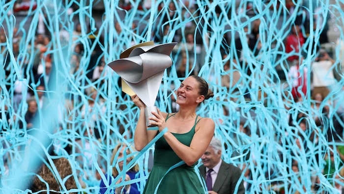 Une joueuse de tennis tient un trophée, des guirlandes tombent tout autour d'elle.