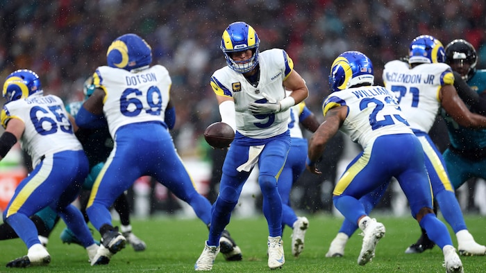 Un quart-arrière avec le ballon est entouré de joueurs de lad équipe dans une séquence offensive.
