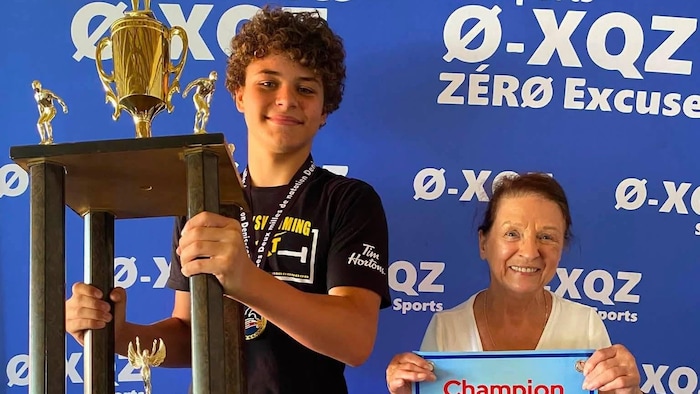 Jeune homme qui tient le trophée en compagnie d'une organisatrice.