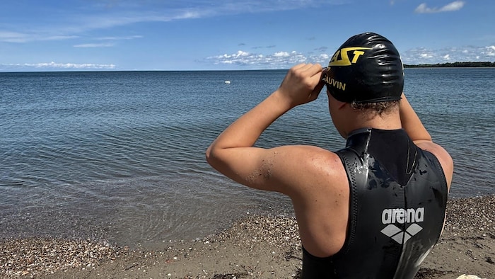 Max, avec un survêtement de nageur, et son casque de natation, est dos au photographe. Il regarde la mer.
