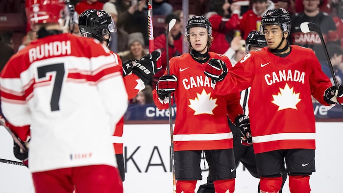 Trois joueurs de hockey rassemblés devant un adversaire. 