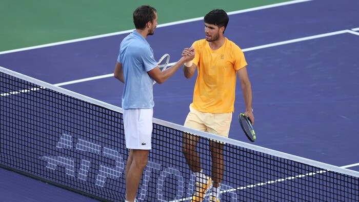 Deux joueurs de tennis se serrent la main au filet. 