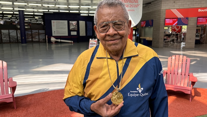 Il tient sa médaille et sourit.