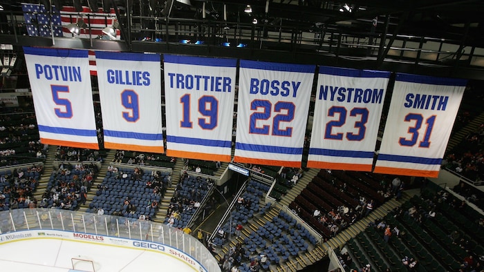Des bannières avec des numéros et des patronymes de joueurs de hockey sont hissées au plafond d'un amphithéâtre.