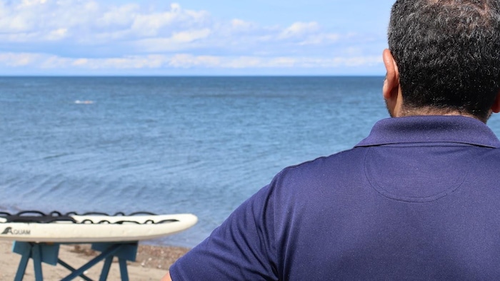 Mohamed Rachidi, de dos, regardant vers le large. Son nageur est au loin.