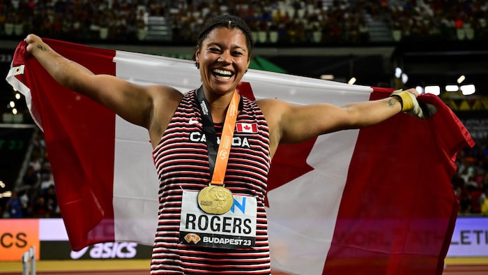 Camryn Rogers sourit avec sa médaille autour du cou et le drapeau canadien sur le dos.