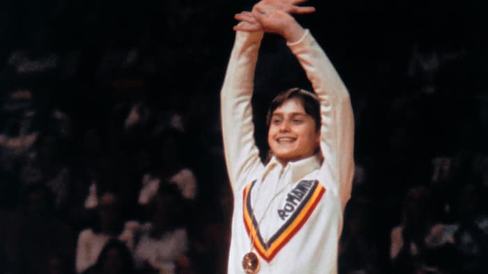 La jeune gymnaste pose avec sa médaille, les bras dans les airs, aux Jeux olympiques de Montréal. 