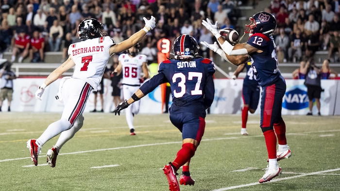 Un joueur de football intercepte une passe devant deux autres joueurs.