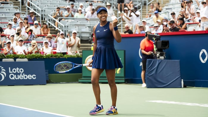 Une joueuse de tennis sourit sur le terrain en serrant le poing gauche.