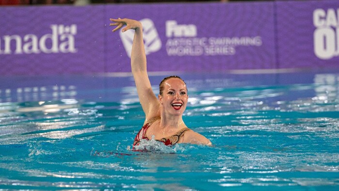 La nageuse tient la pose, le bras levé, dans la piscine.