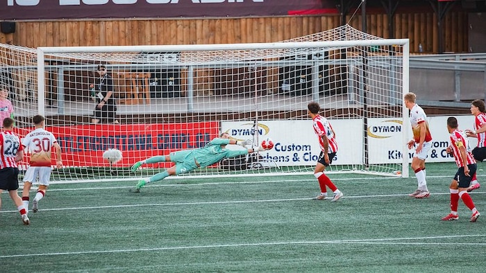 Un gardien plonge et s'étend de tout son long pour effectuer un arrêt pendant un match de soccer.