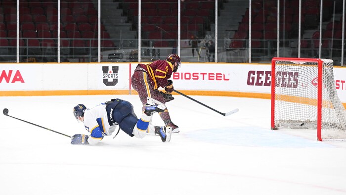 Joueur qui tire dans un filet désert. Un adversaire est couché sur la glace.