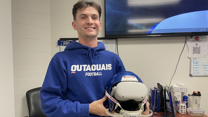 A football coach shows off a helmet equipped with an artificial intelligence system.