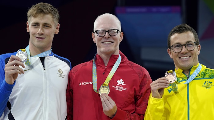 Trois hommes posent sur le podium avec leur médaille. 