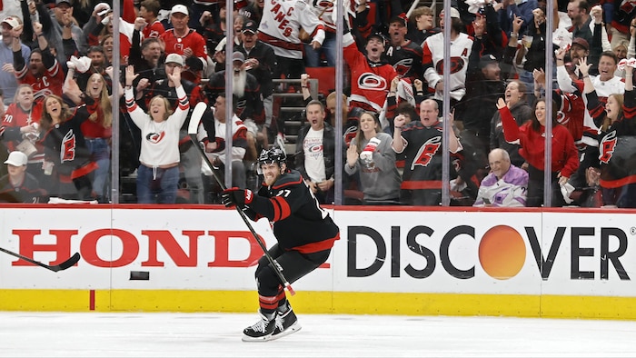 Un joueur de hockey sourit après avoir inscrit un but, la foule derrière lui est en liesse.