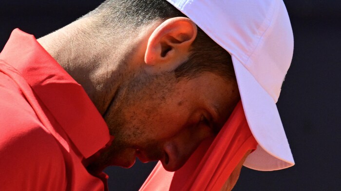 Un joueur de tennis essuie son front avec son chandail.