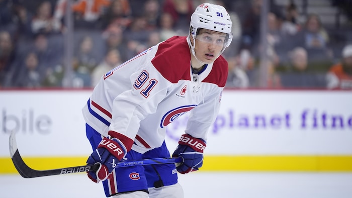 Un joueur de hockey est en attente avec son bâton appuyé sur les genoux.