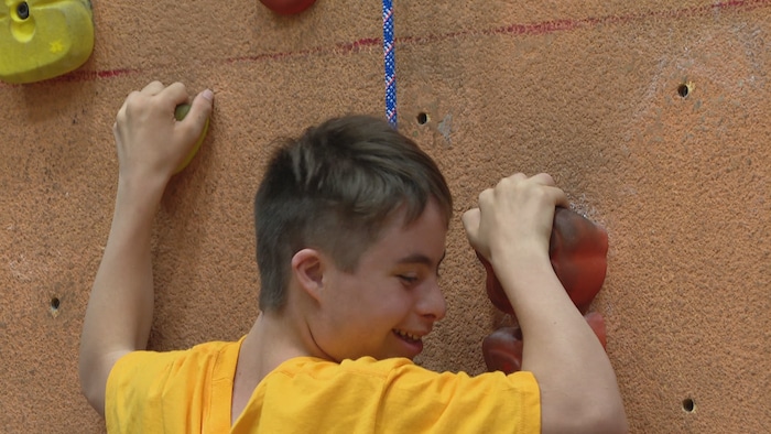 Olivier sourit, accroché au mur.