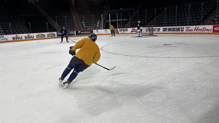Un joueur de hockey, qui est debout, à 45 degré dans sa position vis-à-vis de la patinoire, attend une passe.
