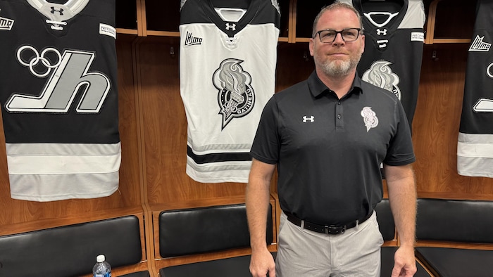 Le nouveau dirigeant d'une équipe de hockey se fait prendre en photo devant les chandails de sa formation.