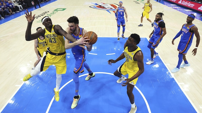 Deux joueurs de basket se disputent le ballon sous le panier, devant les autres joueurs. 