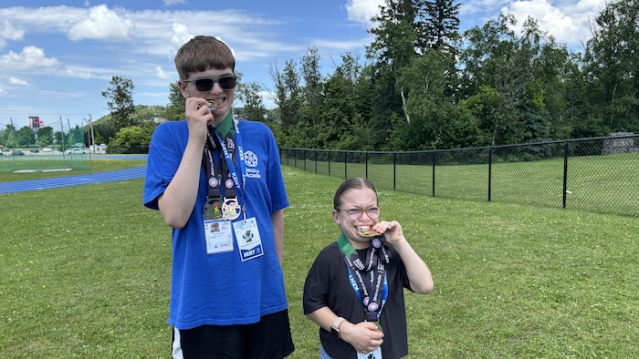 Les deux jeunes prennent la même pose que les athlètes olympiques. Ils mordent une de leurs médailles.