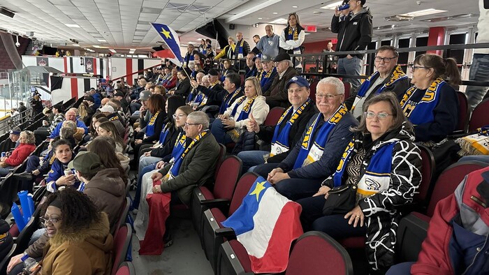 Gens assis dans les estrades avec des drapeaux acadiens et des foulards au couleurs des Aigles Bleus.