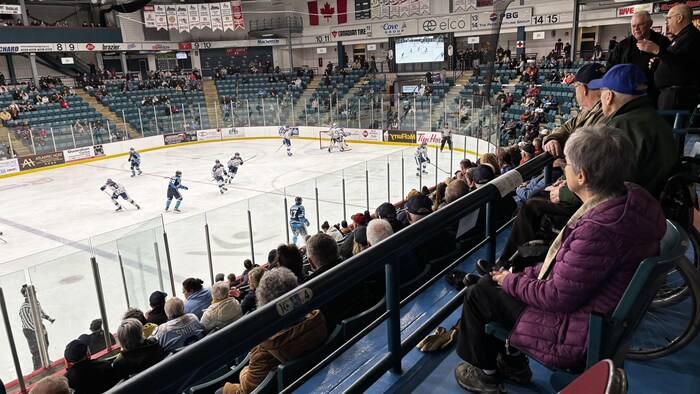 Spectateurs, de biais, qui regardent le jeu sur la patinoire.