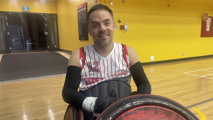 Un homme sourit, assis dans son fauteuil, dans un gymnase.