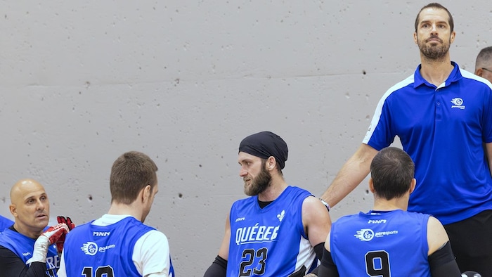 Un entraîneur se tient debout à côté de joueurs en fauteuil roulant.