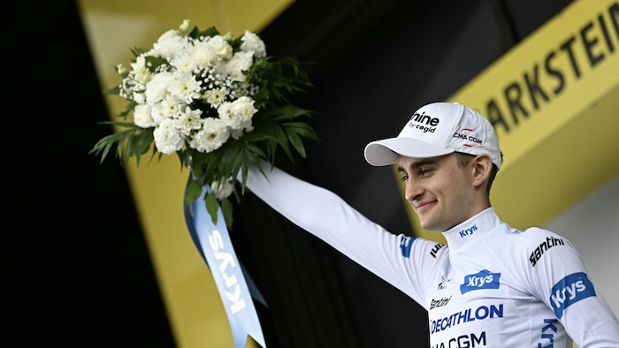 Il porte le maillot blanc sur un podium, après une course.