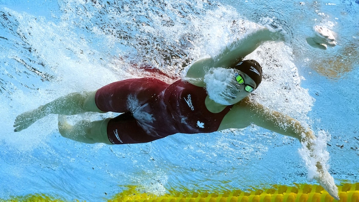 Filmée du fond de la piscine, une nageuse avance dans son couloir, les deux bras en avant.