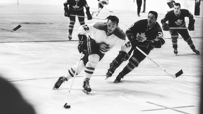 Photo en noir et blanc d'un joueur de hockey qui patine avec la rondelle, un adversaire à ses trousses.