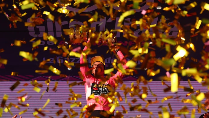Le cycliste Primoz Roglic, entouré de confettis, soulève un trophée en l'air.