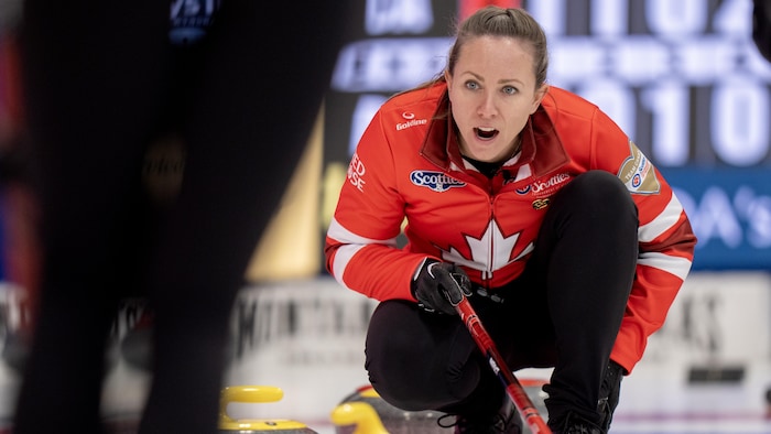 Une joueuse de curling avec son balai, devant des pierres.