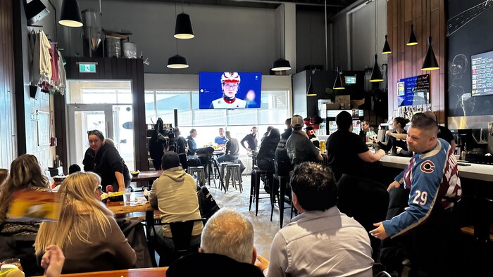 Ils sont assis et regardent une télévision qui montre le visage de Courtney Sarault.