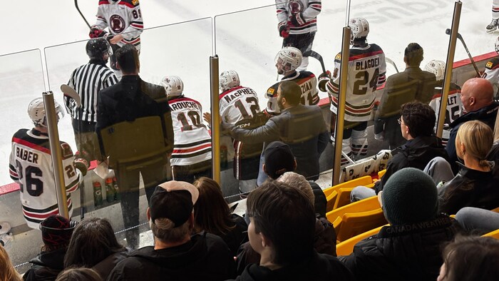 Derrière le banc des joueurs, un homme parle à un arbitre.