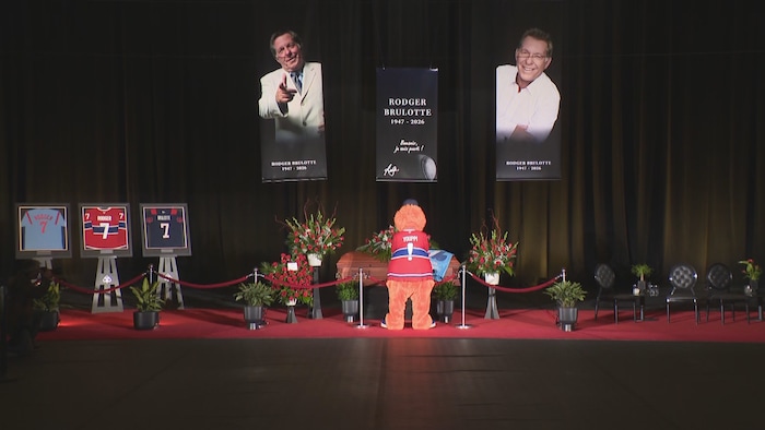 La mascotte se recueille devant le cercueil bordé de fleurs.