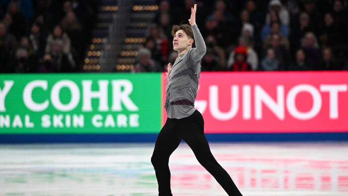 Un patineur artistique regarde vers le haut en faisant une figure sur la glace. 