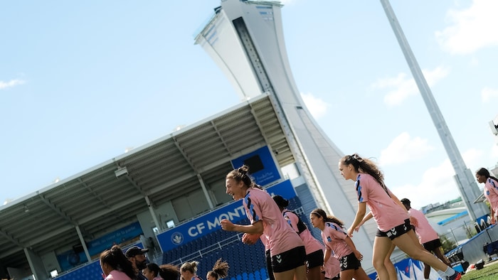 Des joueuses s'échauffent au Stade Saputo, avec le Stade olympique en arrière-plan.
