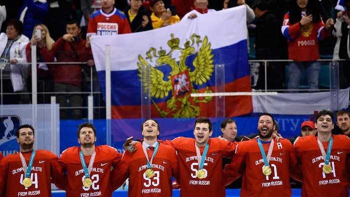 Des hockeyeurs russes se tiennent par les épaules avec la médaille au cou.