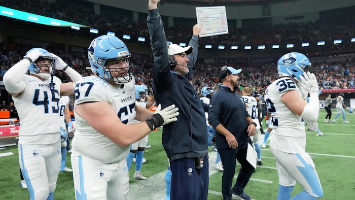 Un entraîneur de football lève les bras au ciel après avoir vu son équipe marquer un touché. 