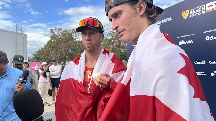 Deux volleyeurs, enveloppés dans des drapeaux canadiens, donnent une entrevue.
