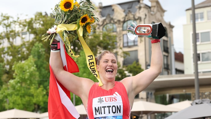 Une femme, souriante, lève un bouquet de tournesols et un trophée.