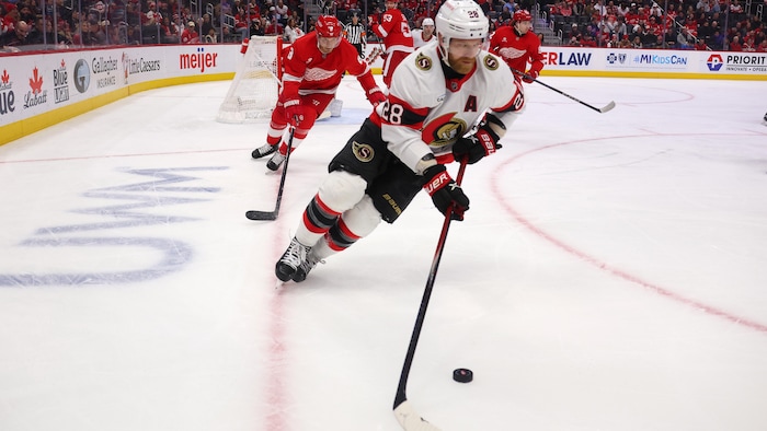 Un joueur de hockey manie la rondelle dans le coin de la patinoire pendant une rencontre.