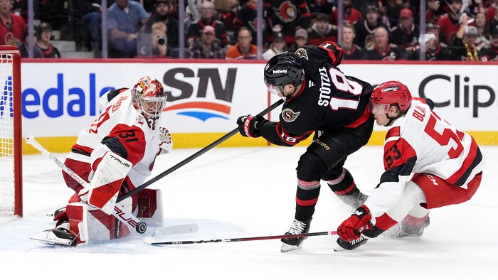 Un gardien de but au hockey fait un très bel arrêt devant un adversaire.