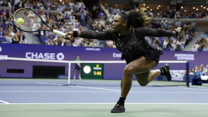 Elle frappe la balle en s'étirant avec son habit noir à paillettes. 