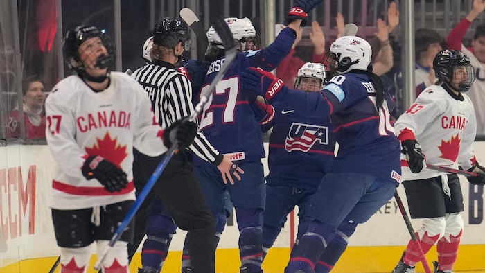 Des joueuses de hockey célèbrent un but devant des adversaires.